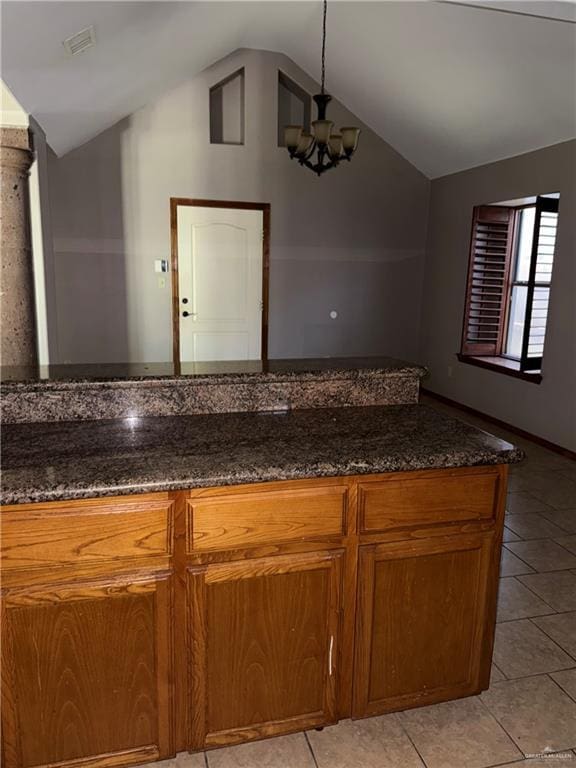 kitchen featuring brown cabinets, a chandelier, dark stone countertops, light tile patterned floors, and lofted ceiling