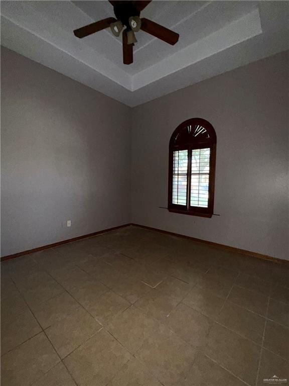 empty room featuring baseboards, light tile patterned flooring, a tray ceiling, and ceiling fan
