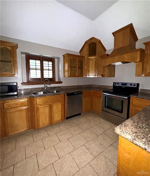 kitchen with lofted ceiling, premium range hood, brown cabinets, a sink, and appliances with stainless steel finishes