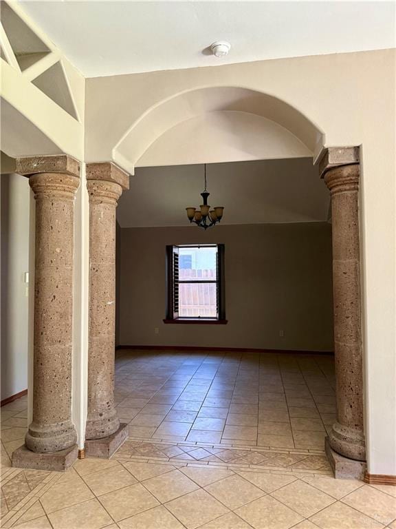 spare room featuring light tile patterned floors, arched walkways, ornate columns, and a chandelier