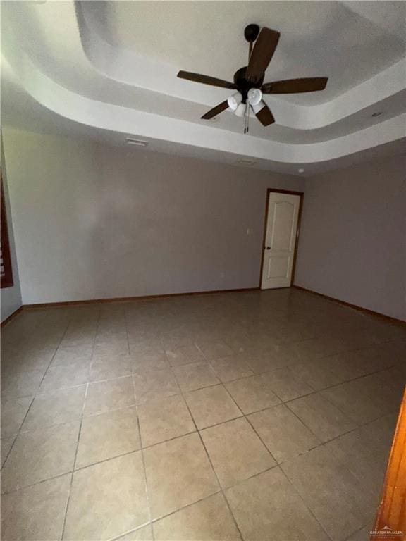empty room with light tile patterned floors, ceiling fan, and a tray ceiling
