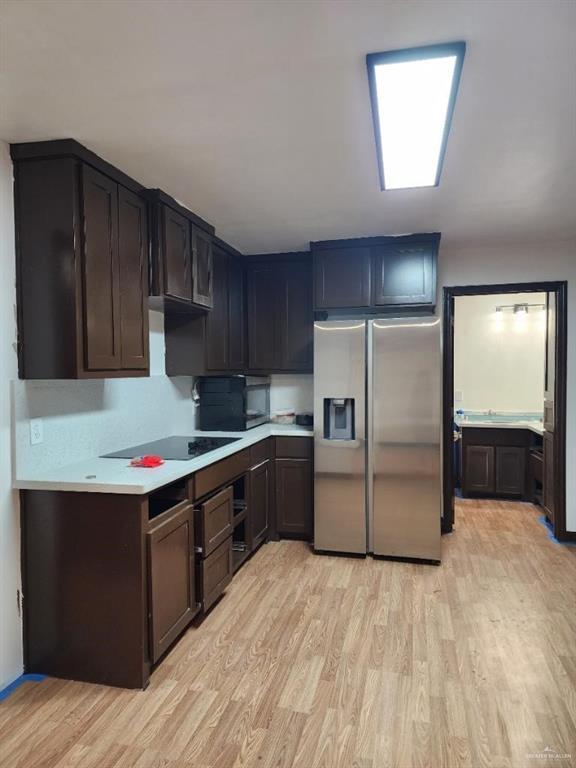 kitchen with light wood-type flooring, dark brown cabinetry, and black appliances