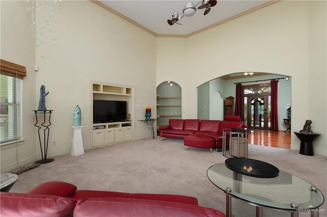 living room with light carpet, built in shelves, a towering ceiling, and ornamental molding