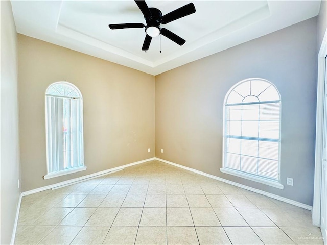 unfurnished room featuring a tray ceiling, light tile patterned floors, and ceiling fan