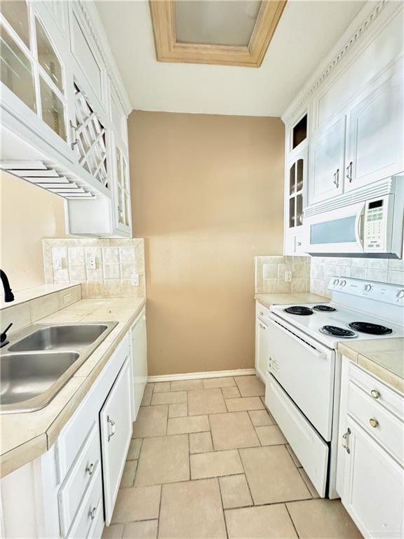 kitchen with sink, white appliances, white cabinets, and decorative backsplash