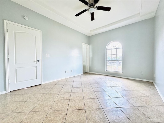 empty room with ceiling fan, light tile patterned floors, and a tray ceiling