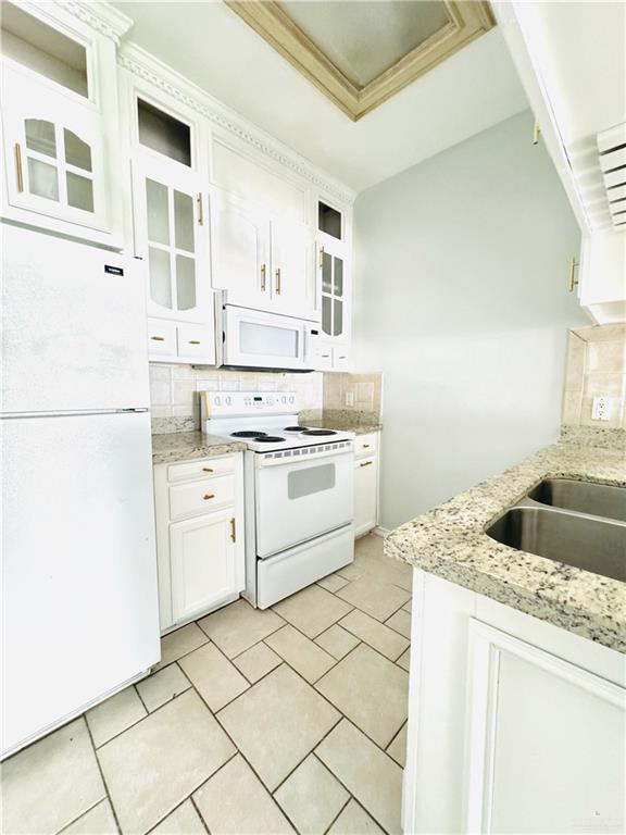 kitchen with white appliances, sink, backsplash, light stone counters, and white cabinetry