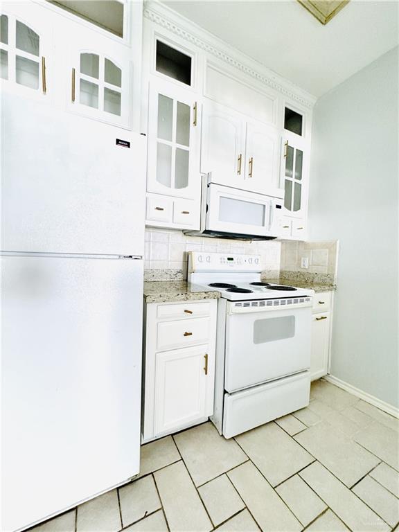 kitchen featuring white appliances, light stone counters, white cabinets, decorative backsplash, and light tile patterned flooring