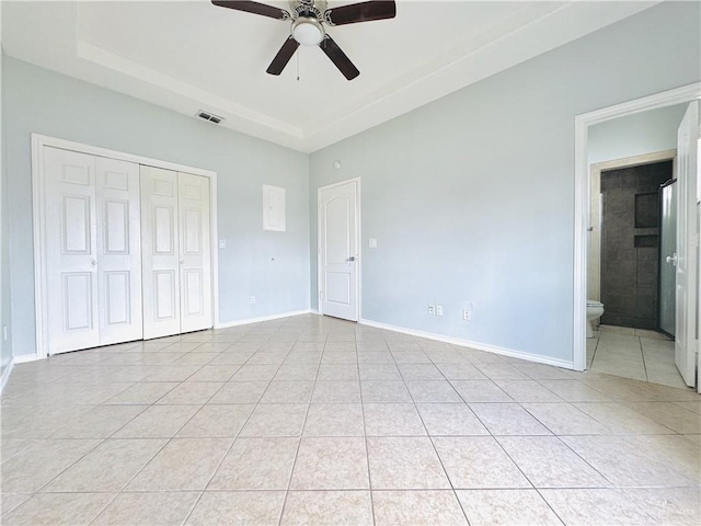 unfurnished bedroom with ensuite bath, a closet, ceiling fan, a raised ceiling, and light tile patterned floors