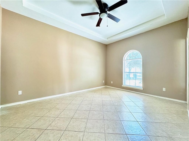 tiled empty room featuring ceiling fan and a raised ceiling