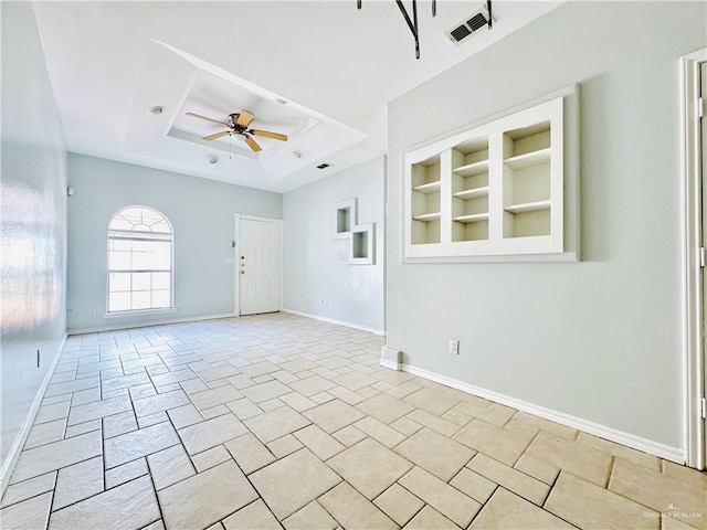 unfurnished room with ceiling fan, a raised ceiling, and built in features