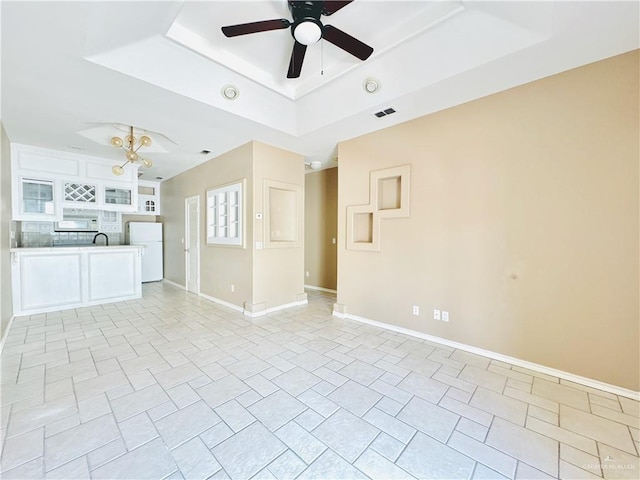 unfurnished living room with ceiling fan with notable chandelier and a raised ceiling