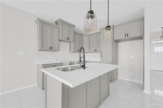 341 Leon Ave, Elsa, TX 78543 - kitchen featuring light marble finish floors, gray cabinets, a center island with sink, decorative light fixtures, and light countertops