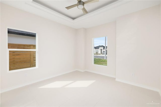 tiled empty room with ceiling fan and a raised ceiling