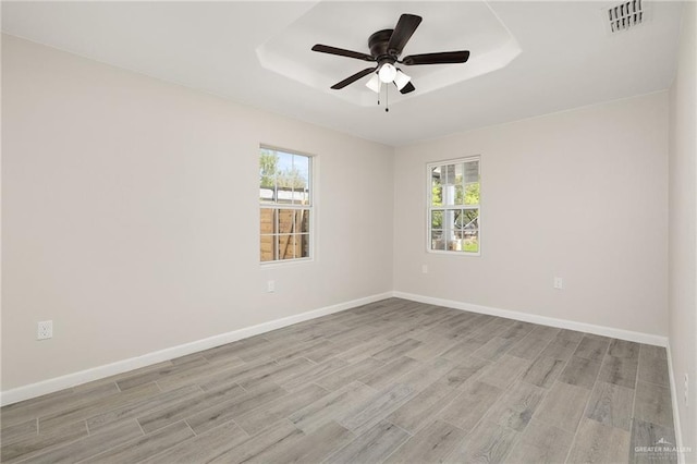 unfurnished room with visible vents, baseboards, light wood-style floors, and a tray ceiling