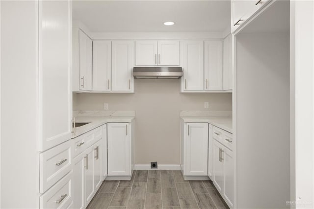 kitchen with baseboards, wood finish floors, under cabinet range hood, light countertops, and white cabinets