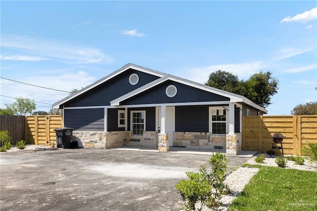 view of front facade featuring a gate, fence, covered porch, and stone siding