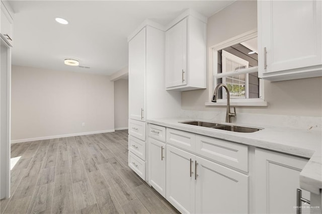 kitchen featuring white cabinetry, light wood-style flooring, light stone countertops, and a sink