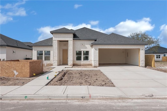 prairie-style house featuring stone siding, concrete driveway, an attached garage, a shingled roof, and brick siding