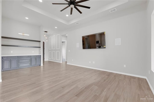 unfurnished living room with a tray ceiling, a ceiling fan, recessed lighting, light wood-style floors, and baseboards
