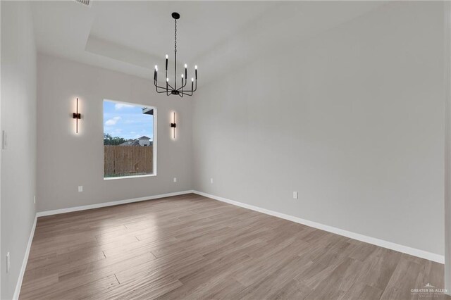 spare room with a chandelier, light wood-style flooring, baseboards, and a tray ceiling