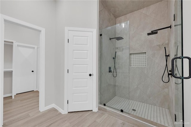 bathroom featuring a stall shower, wood finished floors, baseboards, and a walk in closet