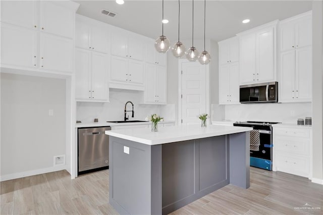 kitchen with appliances with stainless steel finishes, a sink, a center island, white cabinetry, and light countertops