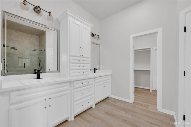 full bath featuring a shower stall, double vanity, wood finished floors, and baseboards