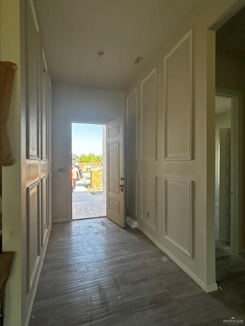 corridor featuring a decorative wall, baseboards, and wood finished floors