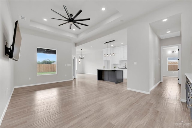 unfurnished living room with a raised ceiling, a chandelier, healthy amount of natural light, light wood-type flooring, and recessed lighting