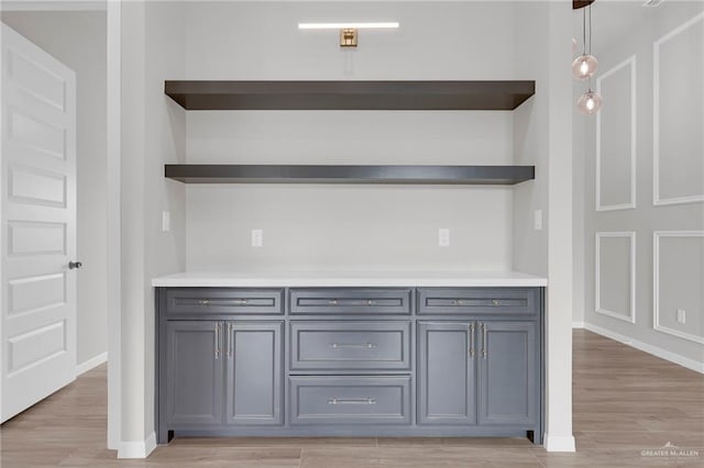 bar with light wood finished floors, baseboards, and pendant lighting