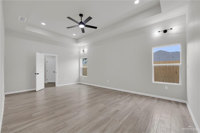 empty room featuring a raised ceiling, ceiling fan, wood finished floors, baseboards, and recessed lighting