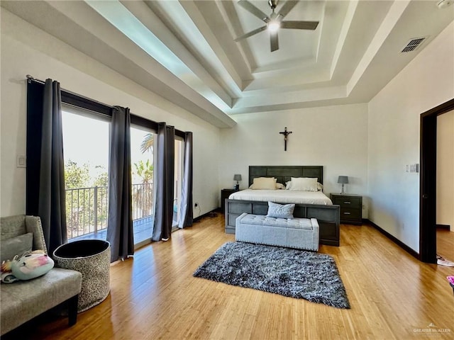 bedroom featuring access to outside, a tray ceiling, light wood-type flooring, and visible vents