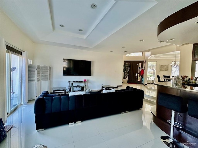 living area featuring light tile patterned floors, a chandelier, a raised ceiling, and french doors