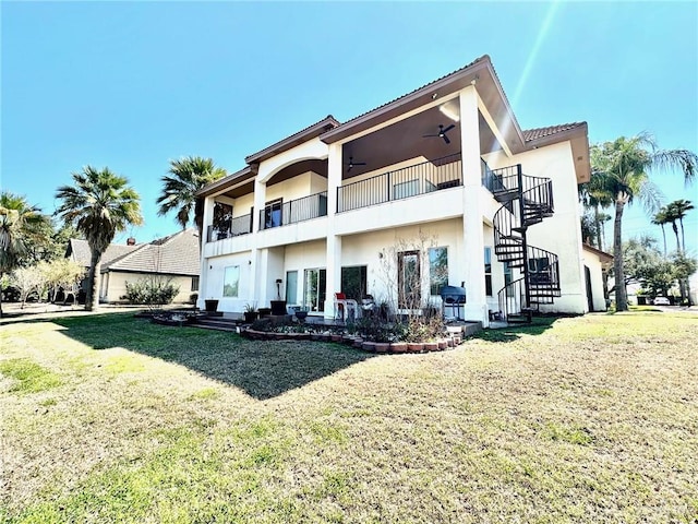 back of property featuring ceiling fan, a balcony, a lawn, stairway, and stucco siding