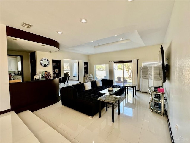 living area with light tile patterned floors, a tray ceiling, visible vents, and recessed lighting