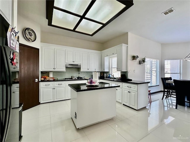 kitchen featuring dark countertops, under cabinet range hood, visible vents, and white cabinets