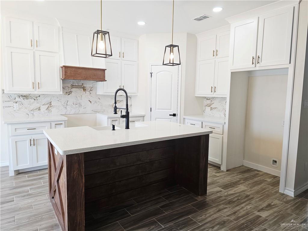 1604 Matilda Rose St, Weslaco, TX 78599 - kitchen featuring wood finished floors, decorative backsplash, a kitchen island with sink, white cabinets, and recessed lighting