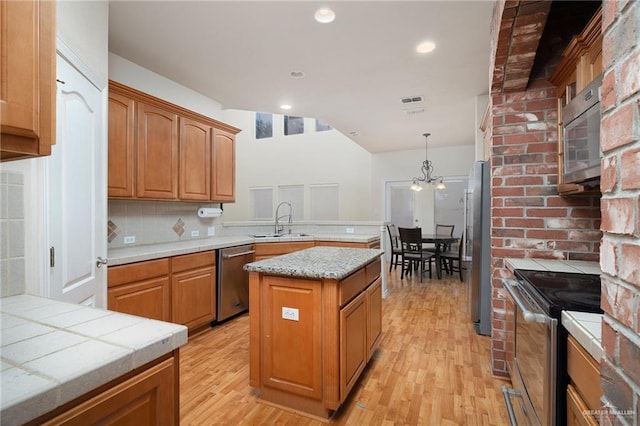 kitchen with pendant lighting, sink, a center island, stainless steel appliances, and light hardwood / wood-style flooring