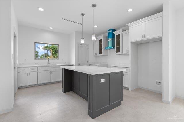 1212 Bridle Way, San Benito, TX 78586 - kitchen with glass insert cabinets, light countertops, white cabinets, recessed lighting, and wall chimney range hood