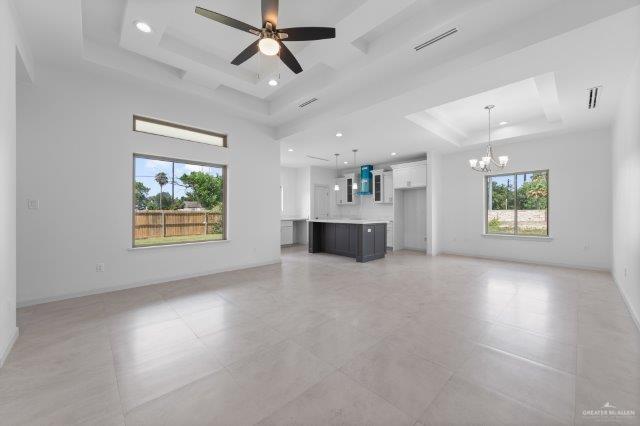 1212 Bridle Way, San Benito, TX 78586 - unfurnished living room featuring a raised ceiling, a chandelier, a ceiling fan, recessed lighting, and baseboards