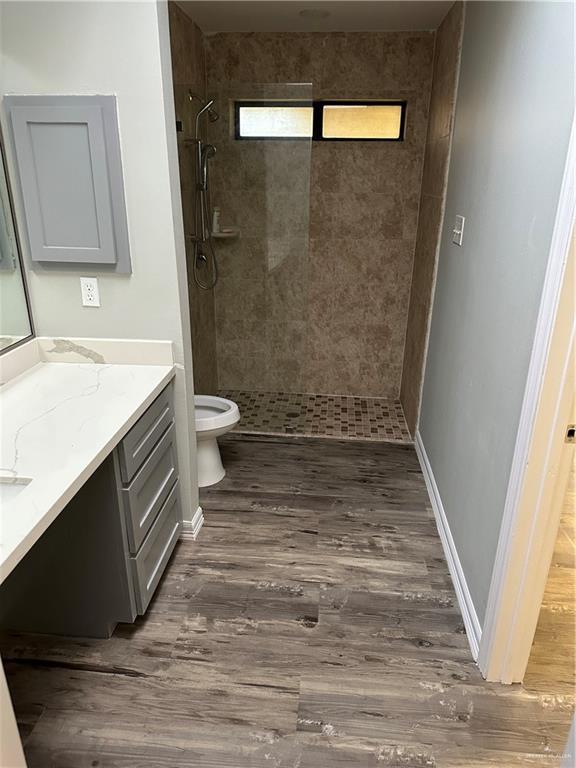 bathroom featuring baseboards, toilet, tiled shower, wood finished floors, and vanity