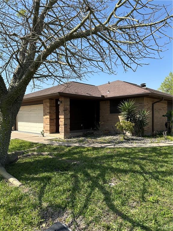 view of front of home with brick siding, an attached garage, a front yard, and roof with shingles