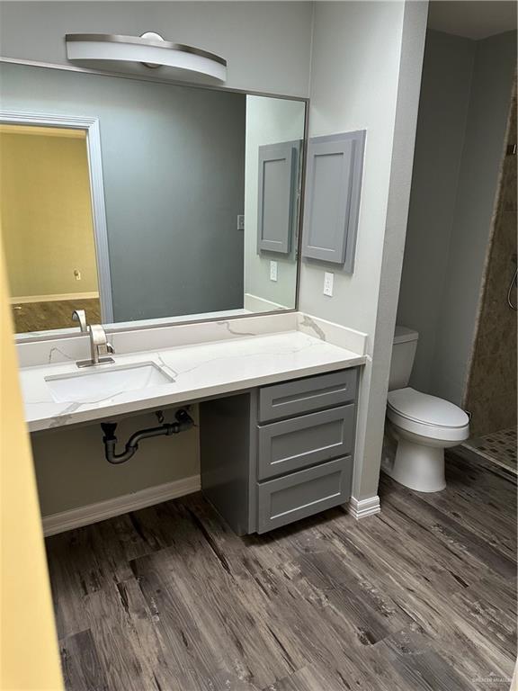 full bathroom with tiled shower, toilet, wood finished floors, and vanity