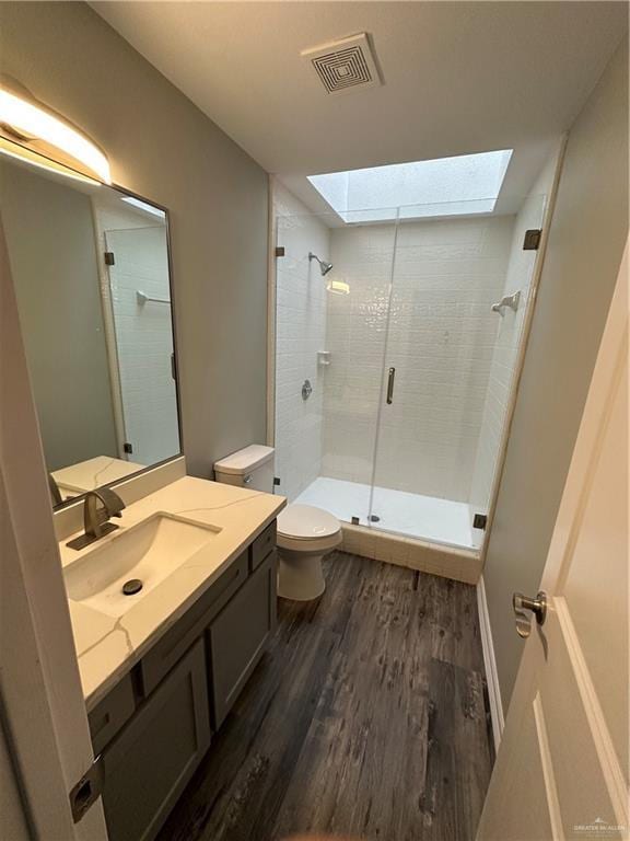 bathroom featuring visible vents, toilet, a stall shower, a skylight, and wood finished floors