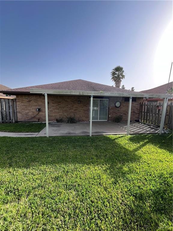 back of property with a patio, fence, a shingled roof, a lawn, and brick siding