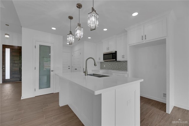 kitchen featuring a center island with sink, white cabinets, hanging light fixtures, and sink