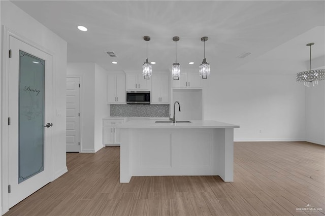 kitchen featuring light hardwood / wood-style floors, white cabinetry, a center island with sink, and sink