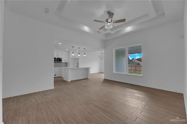 unfurnished living room featuring a raised ceiling, ceiling fan, light hardwood / wood-style flooring, and sink