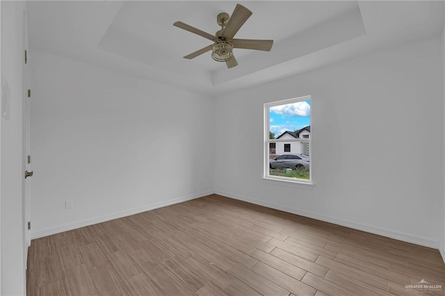 spare room featuring a raised ceiling, light hardwood / wood-style flooring, and ceiling fan